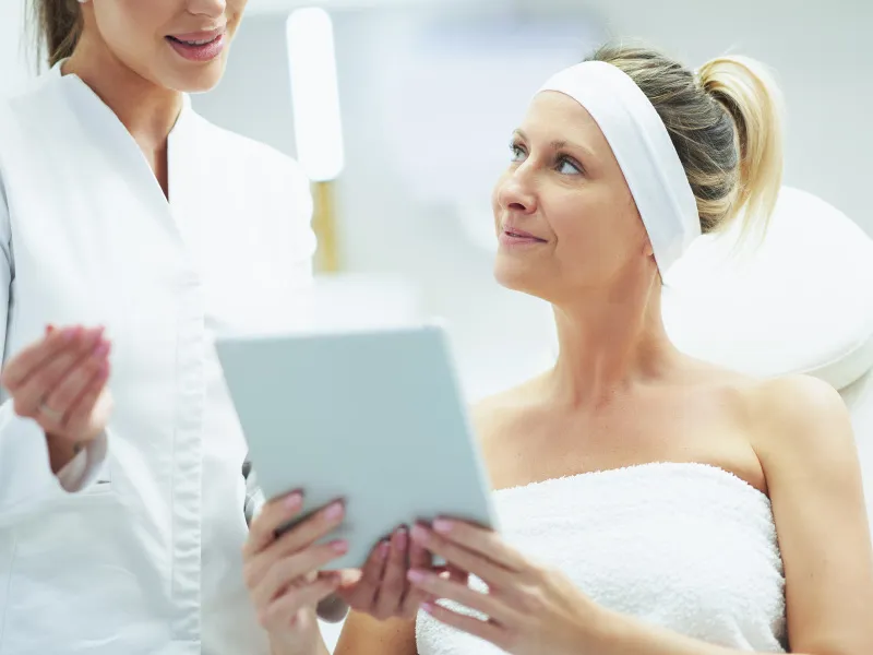 Woman consulting with a dermatologist while reviewing information on a tablet at a clinic