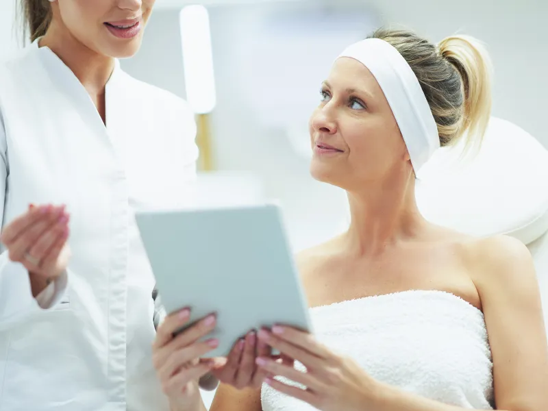 Woman consulting with a dermatologist while reviewing information on a tablet at a clinic